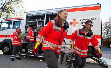BRK Ehrenamtliche helfen bei Katastrophen und Krisen, zwei ehrenamtliche laufen mit einer Kiste