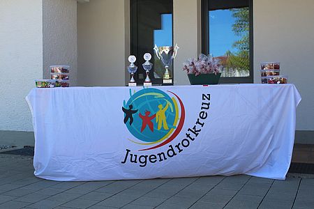 Pokale und Medallien liegen auf dem Tisch, eine Fahne des JRKs hängt vom Tisch