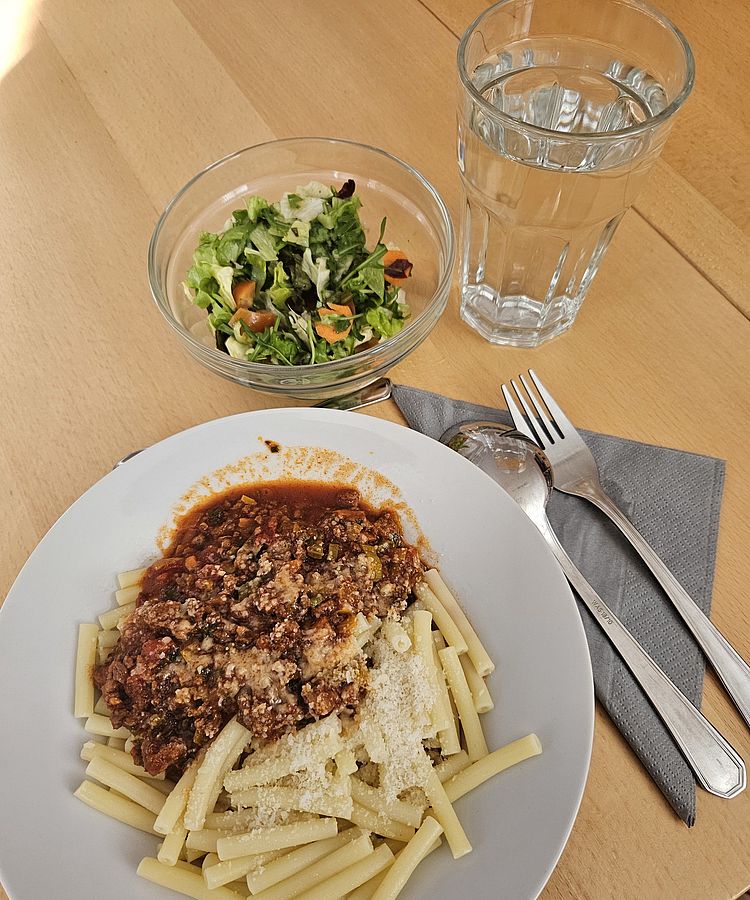 Spaghetti Bolognese mit Salat und ein Glas Wasser
